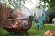 Green lawn chairs face smoky fire pit in backyard