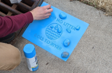 Person using a stencil to promote keeping litter out of a storm drain