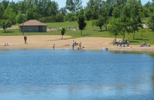 View from the lake looking toward people in the distance on a sandy beach and wading in the water.