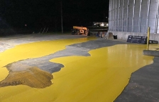 Yellow liquid pools on a cement floor by a metal grain bin.