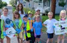 Group of children standing next to a storm drain where they've stenciled "No dumping, drains to lake"