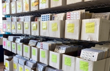 Open top boxes on wire shelves filled with blister packs of prescription medications.