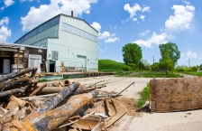 A pile of rusted black metal pipes on the ground with an abandoned corrugated metal building in the background