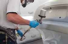 A worker in an auto body shop paints a car using a water-borne finish.