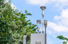 A metal box with saucer-shaped collection instruments on poles attached to the top with trees and blue sky in the background. 