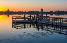 People gathered on a large dock on a still lake at sunset.