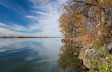 Calm lake reflecting wispy clouds along a rocky shoreline in autumn.