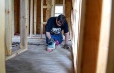 A man using a belt sander on the floor of a building being constructed.