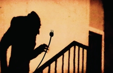 Shadow of a vampire coming up stairs carring a electric cord with fangs. 