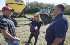 Two men and a woman having a conversation standing next to farm equipment.
