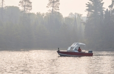 Fishing boat on a calm lake with a hazy tree-lined shore in the background. 