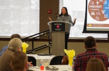 A dark haired woman stands at a podium giving a keynote address.