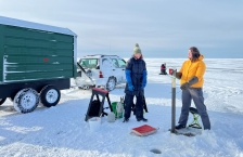 Researchers standing on a frozen lake and collecting samples of sediment from the bottom of the lake