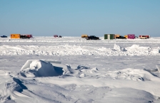 Frozen lake with ice houses and trucks in the distance.