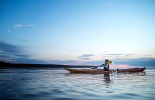 Woman kayaks across a calm lake at sunset.