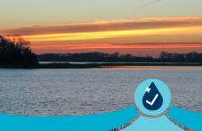 Clouds reflect an orange sunset over a blue lake.