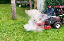 A man on a lawn mower with steam coming out of the front from special equipment attached to the mower. 