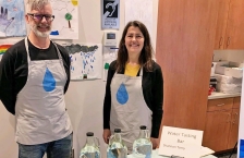 A man and a woman stand behind a table with 3 bottles of water that are used for taste testing samples from different areas of Otter Tail County.