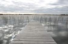 Dock in lake with water reflecting grey cloudy skies.