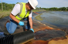 Worker in hard hat and gloves collects water sample.