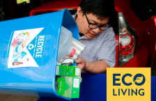 A man pours recycling, including a plastic jug and cardboard boxes, from a small blue bin into a larger one