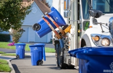 Recycling truck lifting up container along neighborhood curb.