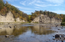 Tall, exposed rock banks line a shallow, rocky river. 