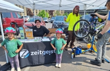 Two young girls wearing bike helmets stand in front of a table with promotional material. 
