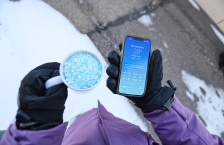 Person holding a cup of de-icing salt and a cellphone showing the temperature.