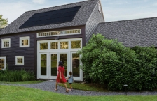A woman and young girl holding hands and walking to the front door of a house with a solar panel on the roof.