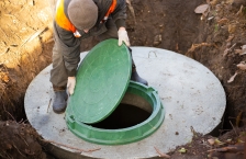 A worker installs a green plastic lid on a septic tank made of concrete.