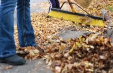 Feet and legs of a person sweeping piles of leaves away from a storm drain.