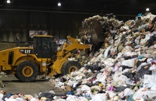 A front-end loader moves piles of bagged trash at a waste facility