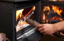 A hand putting a piece of wood into the front door of a wood-burning stove