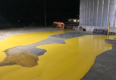 Yellow liquid pools on a cement floor by a metal grain bin.