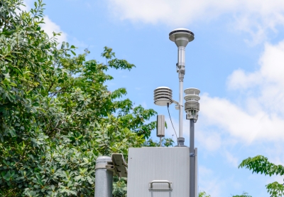 A metal box with saucer-shaped collection instruments on poles attached to the top with trees and blue sky in the background. 
