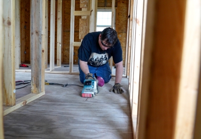 A man using a belt sander on the floor of a building being constructed.