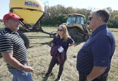 Two men and a woman having a conversation standing next to farm equipment.