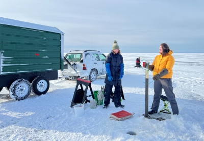Researchers standing on a frozen lake and collecting samples of sediment from the bottom of the lake