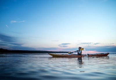 Woman kayaks across a calm lake at sunset.