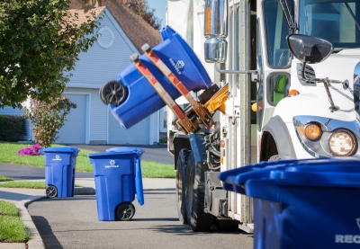 Recycling truck lifting up container along neighborhood curb.