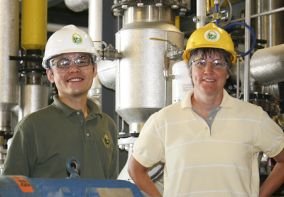 Two people in an industrial setting wearting hard hats