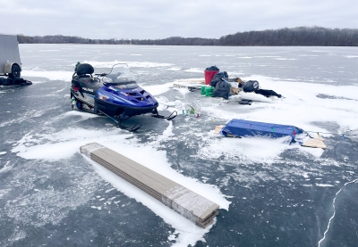 A snowmobile sits next to a pile of garbage on the ice.