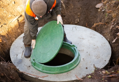 A worker installs a green plastic lid on a septic tank made of concrete.