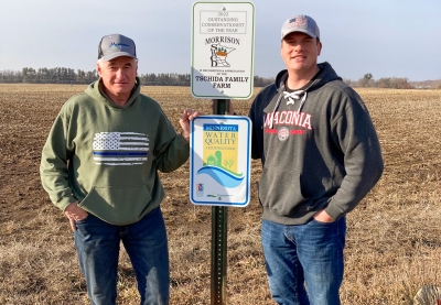 Don Tschida and son standing by signs in field that read "2022 Outstanding Conservationist of the Year" and "Minnesota Water Quality Certified Farm."
