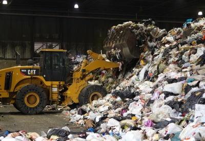 A front-end loader moves piles of bagged trash at a waste facility