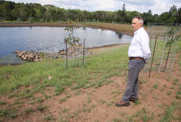 A man stands outside next to a pond in a stormwater garden.