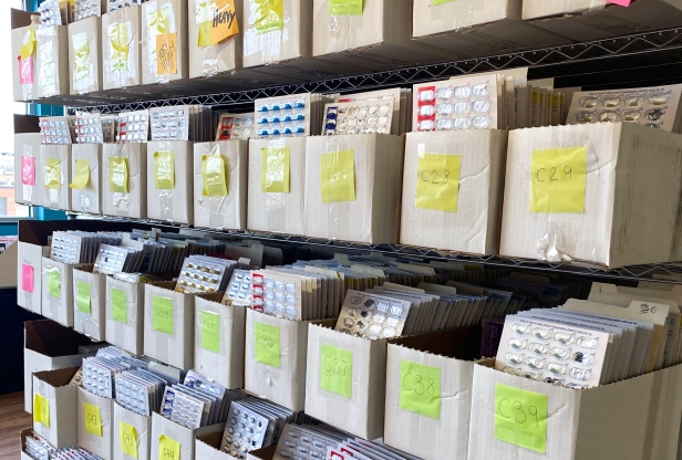 Open top boxes on wire shelves filled with blister packs of prescription medications.