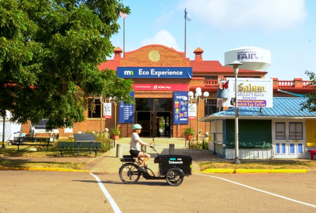 A person riding a cargo e-bike in front of the Eco Experience building at the Minnesota State Fair