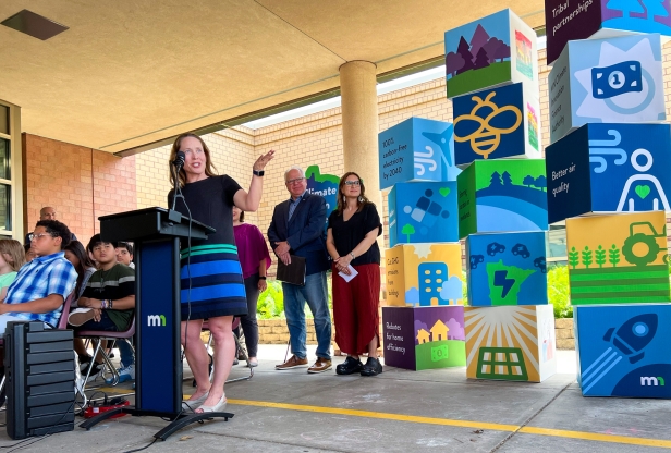 Commissioner Katrina Kessler speaking at a podium, Governor Tim Walz and Lt. Governor Peggy Flanagan stand in the background.